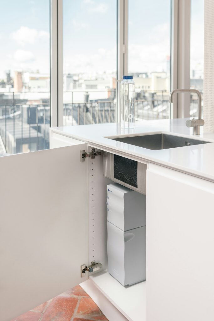 Under kitchen sink organized around plumbing and built-in water filtration system