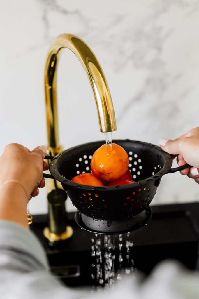 Rinsing fresh tomatoes in a colander under running water