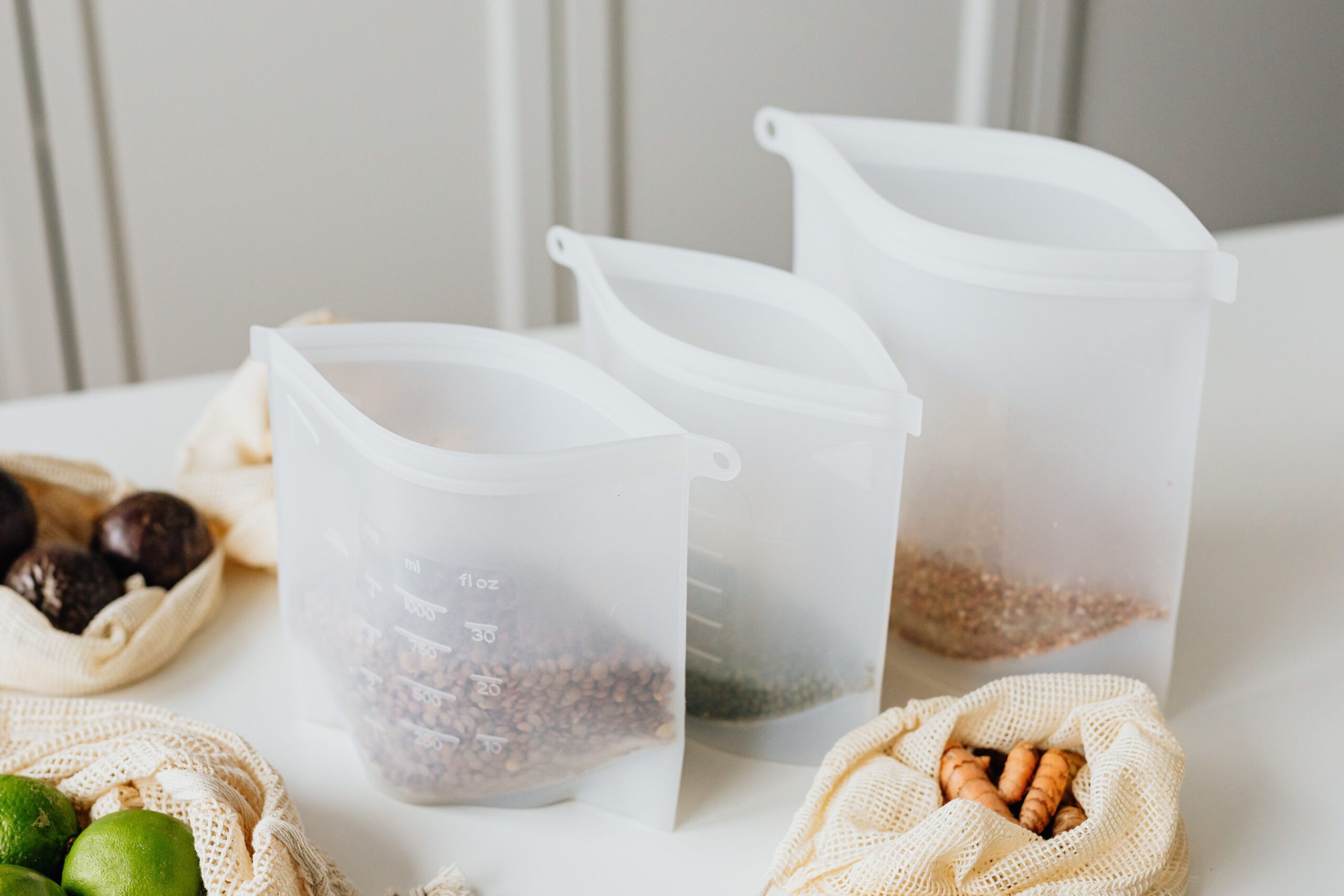 Reusable silicone food storage bags filled with grains and herbs on a kitchen table.