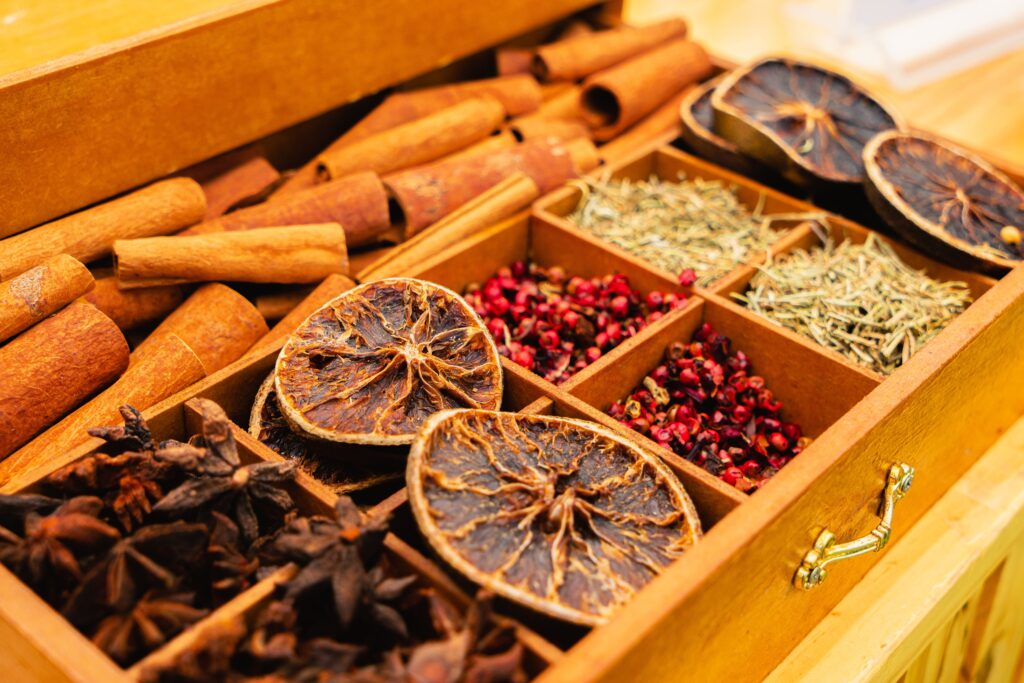Wooden spice organizer box with cinnamon sticks, dried citrus slices, herbs, star anise, and pink peppercorns