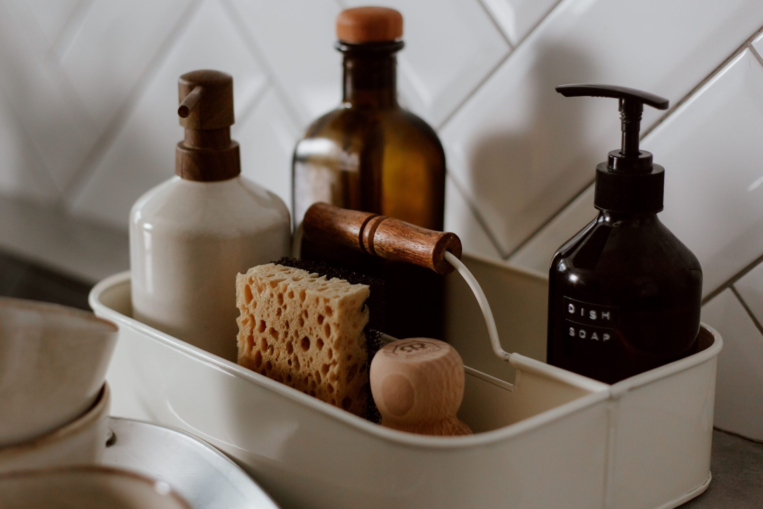 Kitchen sink caddy holding dish soap, sponge, scrub brush, and cleaning bottles beside the sink.