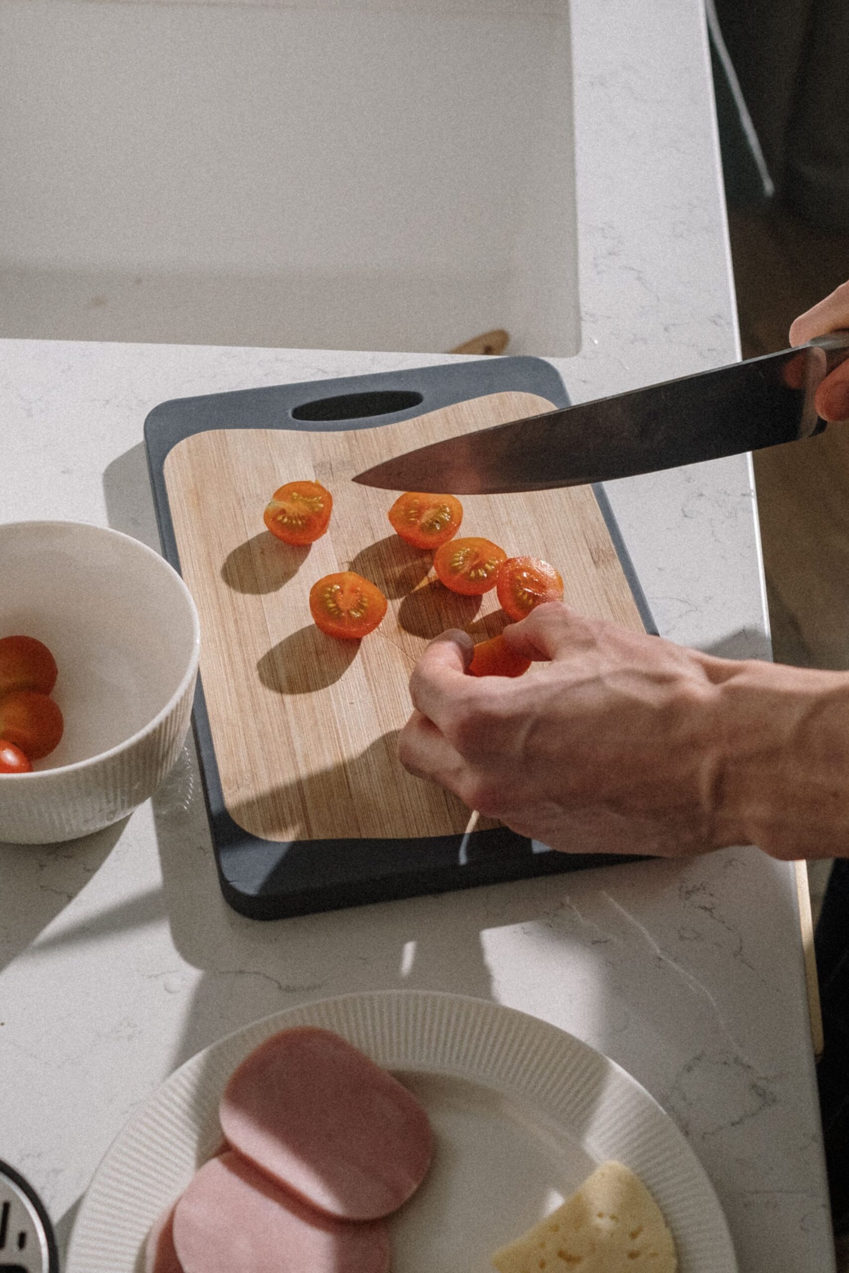 Chopping cherry tomatoes on a cutting board near the kitchen sink