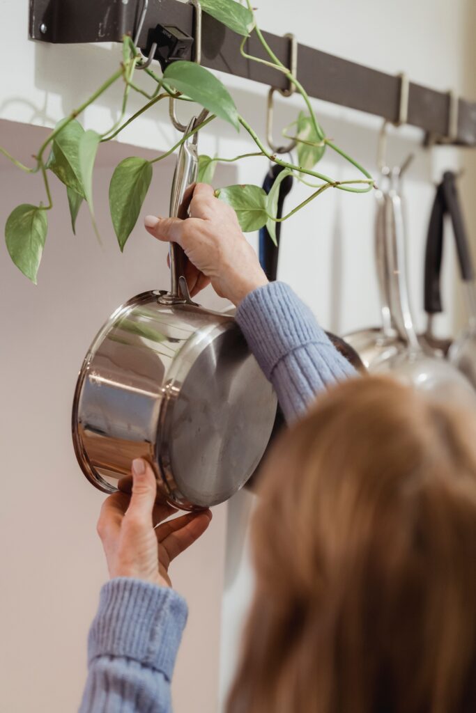 Person hanging a stainless steel cooking pot on a wall-mounted kitchen pot rack with hanging cookware